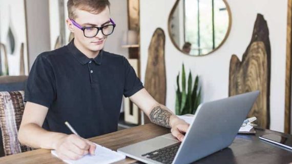 man writing while looking at his laptop