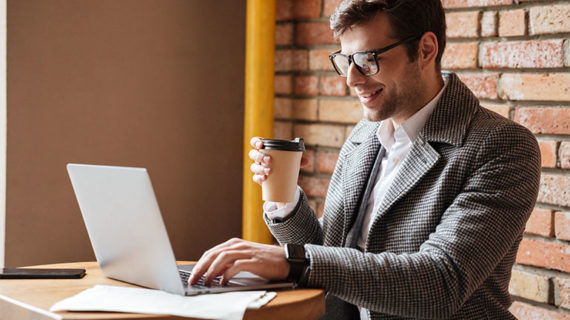 Man reading notes on laptop and drinking coffee