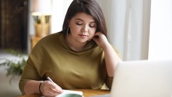 Beautiful plus size young female blogger writing down in her diary