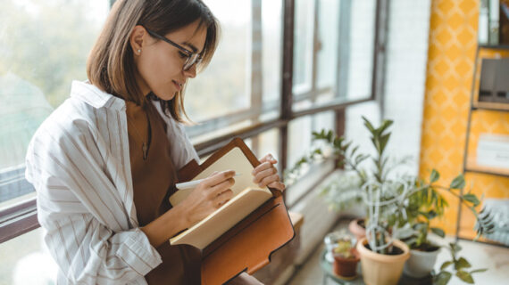 woman writing on her brown notebook