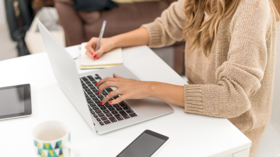 woman taking down notes while using laptop