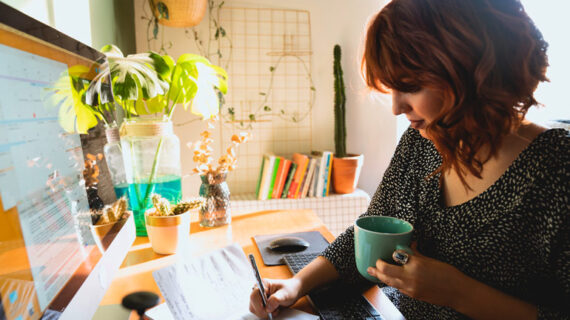 woman with cup taking notes from a computer