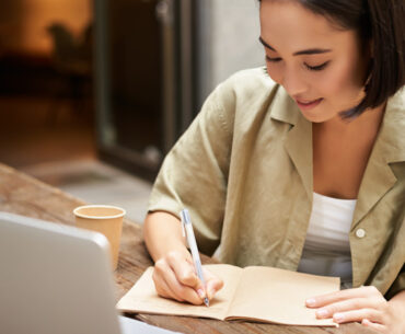 young asian woman working on laptop making notes writing down