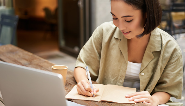 young asian woman working on laptop making notes writing down