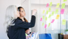 concentrated businesswomen looking at stickers on glass wall