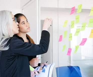 concentrated businesswomen looking at stickers on glass wall