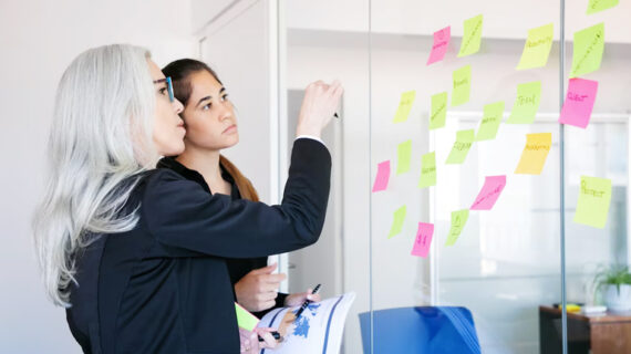 concentrated businesswomen looking at stickers on glass wall