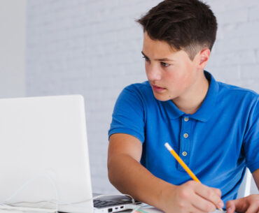 Teenager making notes looking at laptop