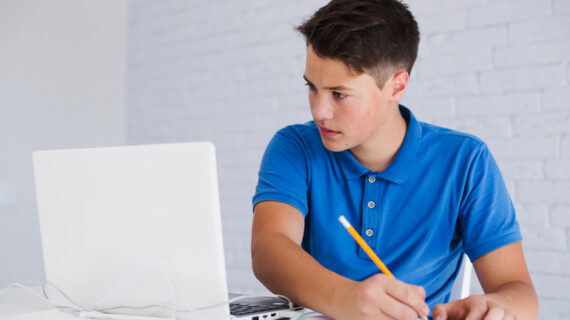 Teenager making notes looking at laptop