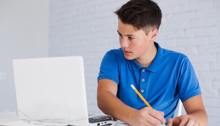 Teenager making notes looking at laptop